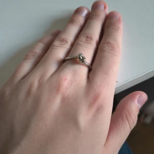 Silverfärgad knutring i minimalistisk stil - En stilren och enkel ring i silverfärg med en snygg knutdetalj framtill. Perfekt för dig som gillar minimalistiska smycken och vill ha något som sticker ut men ändå känns klassiskt. Passar både som statement eller i kombination med andra ringar. Aldrig använd.