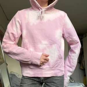 Ljusrosa hoodie med tie-dye - Säljer en ljusrosa hoodie med vitt tie-dye mönster. Tröjan har huva med snörning, stor magficka och ribbade muddar vid ärmslut och nederkant. Perfekt för chill dagar och har en riktigt skön passform. Materialet är mjuk bomull.