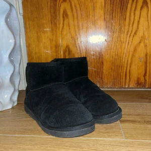 Svarta boots i mocka, storlek 36 - Svarta boots med låg skaft och rund tå, tillverkade i mjuk mocka med fluffigt foder på insidan. Sulan är platt och har ett mönster för extra grepp. Perfekt för kalla dagar och enkel att matcha med olika outfits.