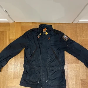 Svart windbreaker från Parajumpers L - Tvär snygg svart windbreaker från Parajumpers med coola detaljer som orange och gul dragflik vid kragen, patch på axeln och flera praktiska fickor med dragkedja. Är i stl L men passar även M mycket bra!🙌✅PRISET GÅR ATT FÖRHANDLA!