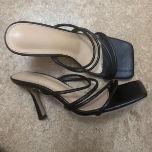 Svarta sandaler med klack och remmar - Stilrena svarta sandaler med hög klack och flera tunna remmar över foten. Storlek 38, använd en/två gånger, så gott som nya. 