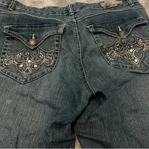 Blå bootcut jeans med broderade fickor - Snygga blå jeans med bootcut passform och detaljerade broderier samt pärlor på bakfickorna. Jeansen har klassisk femficksdesign och är tillverkade i jeansmaterial. Perfekta för dig som vill ha ett par jeans med extra attityd och coola detaljer.