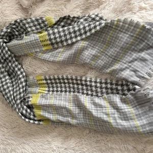 Grå och gul rutig halsduk från Accessories - Snygg halsduk i grått och vitt med rutigt mönster och inslag av gula ränder. Fransiga kanter ger en chill vibe och den är mjuk och skön att ha runt halsen. Perfekt att slänga på sig när det är lite kyligt ute.