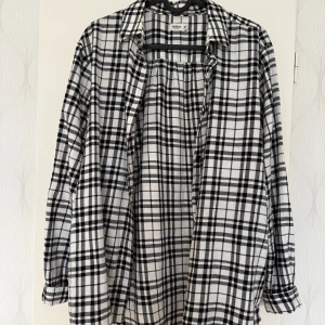 Rutig vit och svart skjorta Dobber XS - Snygg rutig skjorta från MQ i storlek XS. Skjortan är vit med svarta rutor, har klassisk krage och långa ärmar med knappar vid manschetten. Mjuk bomullskänsla och loose fit för chill vibe. Perfekt att slänga över en t-shirt.