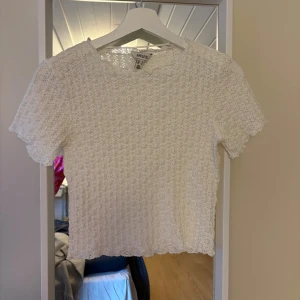 Vit t-shirt - Säljer en söt vit blus från AWARE i storlek S. Toppen har korta ärmar och är helt täckt av ett fint spetsmönster med vågig kant vid halsringningen. Aldrig använd!💕