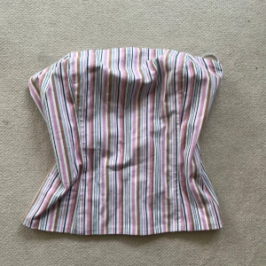 Randig korsett från mango i rosa och beige - Säljer en snygg randig korsett från mango i storlek M. Toppen har ränder i rosa, beige, vitt och blå, med en smickrande form och dragkedja bak. Aldrig använd. 