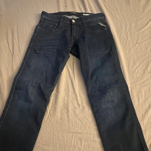 Mörkblå Replay Anbass jeans slim fit - Snygga mörkblå jeans från Replay, modell Anbass med slim fit. Klassisk femficksdesign, diskret Replay-logga på fickan och bak, samt läderpatch i midjan. Jeansen är tillverkade i stretchig denim för en bekväm passform.