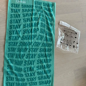 Convini grön huvudbonad - Multifunktionell huvudbonad i ljusgrön färg med texten "STAY SHARP" upprepad över hela tyget. Den levereras i en plastförpackning som visar olika sätt att bära den.