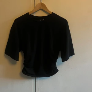 Svart croppad topp från Gina Tricot - En svart croppad topp med vida ärmar och rund halsringning. Den har lös passform upptill och blir tajtare nertill. Den är i ett skönt och luftigt material. Supersnygg!!