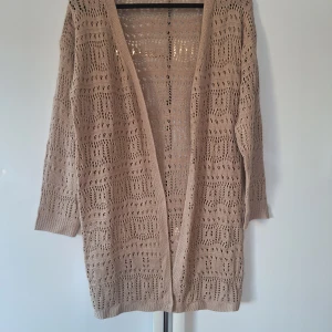 Beige stickad kofta med hålmönster M/L - Säljer en beige stickad kofta med öppen front och snyggt hålmönster. Koftan har lång ärm och är perfekt att slänga över en topp för en chill och stilren look. Lätt och luftig, passar grymt till både jeans och klänning.