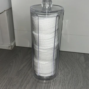 Bomullsrondeller i genomskinlig burk - Runda vita bomullsrondeller i en hög, genomskinlig plastburk med lock. Perfekt för att ta bort smink eller applicera toner. Enkel och stilren förvaring som passar på sminkbordet. Pris diskuteras. Och ej använt.
