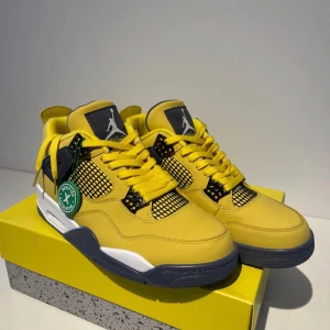 Nike Air Jordan 4 tour yellow - Nike Air Jordan 4 Retro sneakers i en riktigt fet gul färg med svarta och vita detaljer. Skorna har klassisk meshpanel, Jumpman-logga på hälen och tungan samt robust snörning. Ovandelen är i skinn och sulan är vit och svart med gul logga undertill. Perfekta för dig som vill sticka ut.använd bara en gång
