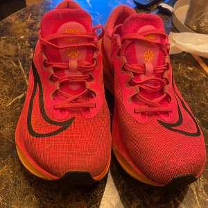 Nike Zoom fly X löparskor - Nike Zoom Fly 5 sneakers i en riktigt snygg rosa färg med orange sula och svarta detaljer. Skorna har mesh-överdel för bra andningsförmåga, snörning och en tjock, responsiv sula som passar perfekt för löpning och träning. Ikonisk Nike-logga på sidan och coola detaljer på plösen. Nypris 2000. Använda 4 gånger