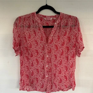 Röd paisleymönstrad skjorta Indiska - Paisleymönstrad skjorta från Indiska i rött och vitt. Skjortan har korta ärmar med lätt puff, knappar framtill och en luftig, avslappnad passform. Perfekt för dig som gillar färg och mönster. Tunn och skön, passar till många olika stilar.🤩💕