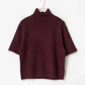 Vinröd stickad polotröja kort ärm - Mysig vinröd stickad polotröja med korta ärmar och hög krage. Tröjan har en loose passform och är perfekt för lager-på-lager. Materialet är mjukt och ger en chill vibe till outfiten. ALDRIG ANDVÄND