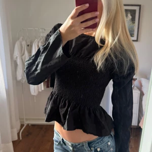 Svart blus med volang - Svart blus med långärmade ärmar, tight passform. Blusen är i storlek small och har en volang nertill 