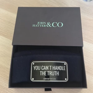 Mörkblå mössa John Hatter & Co - Pris kan diskuteras: droppas av vart som i Stockholm.      Cool svart mössa från John Hatter & Co med uppvikt kant och en metallskylt framtill med texten 'YOU CAN'T HANDLE THE TRUTH'. Mössan är stickad och har en stilren, urban vibe som sticker ut. Perfekt accessoar för dig som gillar statement-plagg.