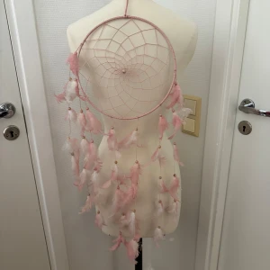 Stor rosa drömfångare -  Drömfångare med rosa fjädrar. Stor som ni ser i jämförelse med ”provdockan”. Hämtas i Hägersten om du vill slippa frakt. Var även uppmärksam på när Plick erbjuder fraktfritt ibland på dyrare plagg. Följ mig gärna. Har mycket att lägga ut i olika storlekar! 