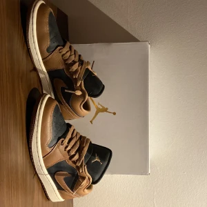 Nike Air Jordan 1 Low brun/svart - Säljer ett par Nike Air Jordan 1 Low i brun och svart med klassisk vit sula. Skorna har snygga bruna läderdetaljer med skolådan. Pris kan diskuteras