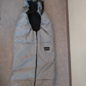 Ljusgrå åkpåse från Beemoo - Säljer en ljusgrå åkpåse från Beemoo med dragkedja framtill och praktiska öppningar för sele. har en hög krage med snörning och är fodrad med svart tyg på insidan. Perfekt för kalla dagar och enkel att använda i barnvagn.