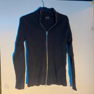 Svart ribbad kofta från Only & Sons - Säljer en svart ribbad kofta från Only & Sons med hel dragkedja framtill och hög krage. Tröjan är långärmad och har en stilren, smal passform. Perfekt för lager-på-lager och enkel att matcha med andra plagg.