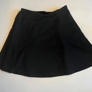 Svart kortkjol från Cubus - Enkel och stilren svart kortkjol från Cubus i A-linjeformad modell. Kjolen har en slät midja och är sydd i ett mjukt tyg som ger en snygg siluett. Perfekt att matcha med en crop top eller stickad tröja.