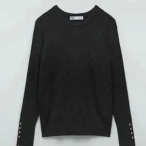 Svart stickad tröja från Zara - Svart stickad tröja från Zara med rund halsringning och långa ärmar. Snygga silvriga knappar längs ärmsluten ger en stilren touch. Perfekt till jeans eller kjol för en clean look💕