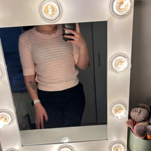 Ljusrosa stickad topp från 157 - Supersöt ljusrosa stickad topp från 157 med korta ärmar och rund hals. Tröjan har ett genombrutet, virkat mönster och är gjord i 100% bomull. Perfekt för vår och sommar när du vill ha en chill och fräsch look.