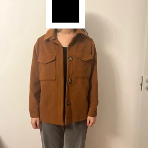 Brun overshirt med stora fickor - Snygg brun overshirt med stora bröstfickor och knappar framtill. Jackan har klassisk krage och raka ärmar, perfekt för lager-på-lager. Materialet känns mjukt och har en ullig look. Enkel och stilren design som passar till det mesta.