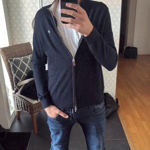 Mörkblå merinoull helzip från Morris - Säljer en stilren mörkblå kofta från Morris i 100% merinoull. Koftan har dragkedja framtill, broderad logga på bröstet och ribbade muddar. Perfekt för dig som vill ha en klassisk och snygg look med premiumkänsla. Passar även storlek S!!!
