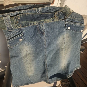 Jeanskjol med bälte och fickor - Snygg jeanskjol i klassisk blå denim med coolt bälte i midjan och silvriga nitar. Kjolen har framfickor med tryckknappar och en rak, kort passform. Perfekt för dig som gillar en avslappnad och trendig stil.