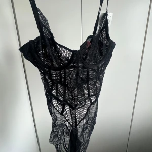 Svart spetsbody från Hunkemöller - Svart spetsbody från Hunkemöller med prislapparna kvar, i återvunnen nylon med transparent spets och mesh. Justerbara axelband, dekorativa sömmar och fina spetsdetaljer. Den är aldrig använd men testad på en gång, knäppte den inte då den var för liten upptil på mig. Perfekt för dig som gillar snygga underkläder med en lyxig känsla.