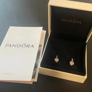 Pandora örhängen med rosa hjärtan - Supersöta örhängen från Pandora i silver med gnistrande rosa hjärtformade stenar och små vita stenar runtom. Kommer i originalask och med Pandora-kort. Perfekta för dig som älskar romantiska detaljer och vill sticka ut lite extra.
