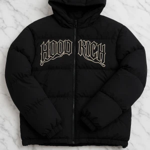 Svart pufferjacka från Hoodrich - Säljer en svart pufferjacka från Hoodrich med stor broderad logga på bröstet. Jackan har huva, dragkedja framtill och elastiska muddar vid ärmslut och nederkant. Perfekt för kalla dagar och streetwear-stil.