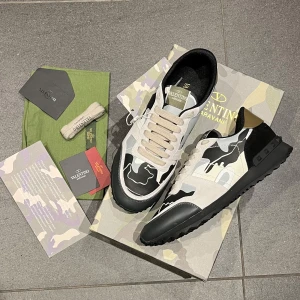 Valentino Garavani Rockrunner sneakers - Snygga Valentino Garavani Rockrunner sneakers med svart, beige och grått camouflagemönster. Skorna har snörning, platt sula och detaljer i skinn och mocka. Ikonisk design med guldtonad häl och robust yttersula. Perfekta för dig som vill sticka ut med stil.