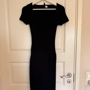Svart ribbad långklänning H&M - Svart ribbad långklänning från H&M med fyrkantig ringning och korta ärmar. Klänningen har en tight passform och är tillverkad i stretchigt material som sitter snyggt på kroppen. Perfekt för dig som gillar en stilren och enkel look.