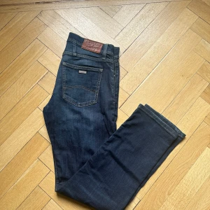 Armani Exchange J16 raka jeans blå - Snygga mörkblå jeans från Armani Exchange, modell J16 Straight. Klassisk femficksdesign med raka ben och kontrastsömmar. Jeansen har en läderpatch med logga bak i midjan och är tillverkade i mjukt denimtyg.