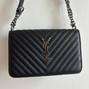 Svart axelväska - Säljer en svart axelväska med klassiskt silverfärgat logospänne framtill. Perfekt för dig som vill ha en stilren och lyxig accessoar.