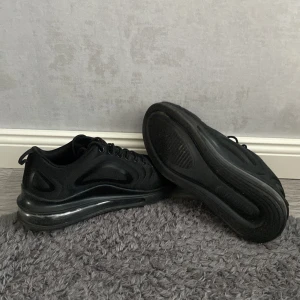 Svarta Nike Air Max sneakers strl 41 - Säljer ett par helsvarta Nike Air Max sneakers med snygg, futuristisk design och tydlig Air Max-sula. Skorna har snörning, diskret vit swoosh och är tillverkade i syntetmaterial. Perfekta för dig som gillar sportig och clean stil.