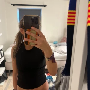 Svart ärmlös croppad topp - Säljer en svart, tight och croppad ärmlös topp med hög hals. Perfekt för dig som gillar en enkel och stilren look. Toppen är i mjukt material och sitter snyggt mot kroppen.