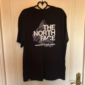 The North Face T-shirt - Svart t-shirt från The North Face med stor vit logga och bergmotiv på ryggen samt liten logga på bröstet. Klassisk passform och rund hals. Tillverkad i mjuk bomull, perfekt för en avslappnad streetstyle.