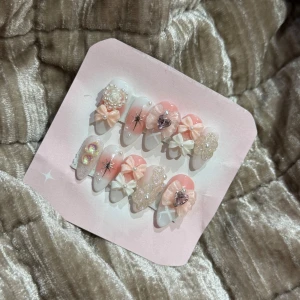 Söta rosa och vita lösnaglar med dekorationer - Supergulliga lösnaglar i rosa och vitt med 3D-dekorationer som pärlor, rosetter, blommor och hjärtan. Naglarna har glittriga detaljer och små stenar för extra bling. Perfekt för dig som vill ha en kawaii och lyxig nagel-look.