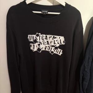 Svart sweatshirt från Just Cavalli - Cool svart sweatshirt från Just Cavalli med vit, trasig textprint framtill. Tröjan har rund halsringning och långa ärmar. Perfekt för dig som gillar streetstyle och vill sticka ut med en unik design.