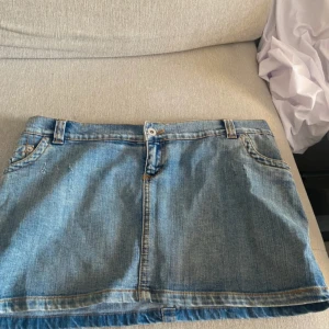 Blå jeanskjol i klassisk modell - Säljer en blå jeanskjol i klassisk femficksmodell med bälteshällor och snygga kontrastsömmar. Kjolen är kort och har en rak passform, perfekt till sneakers eller boots. Stängs med knapp och dragkedja framtill.