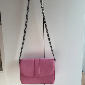 Gina Tricot rosa axelväska i mocka-look - •Snygg rosa axelväska med kedjerem och magnetlås. •Väskan har en stilren design med flera fack inuti och är gjord i ett material som liknar mocka.  •Perfekt storlek för det viktigaste och ger en trendig touch till din outfit. •Mycket bra skick. •Djurfritt och rökfritt hem.