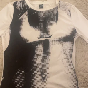 Vit långärmad topp med tryck från SHEIN - Säljer en vit långärmad topp från SHEIN med ett svart grafiskt tryck som föreställer en kropp. Tight passform och rund halsringning. 