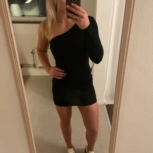 One shoulder klänning - Jättesnygg svart klänning. Den är figursydd och går in vid midjan med jättefina detaljer. Helt ny, aldrig använd. Prislappen sitter kvar.