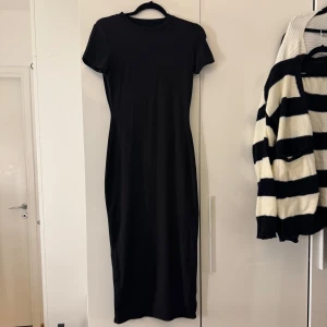 Svart klänning  - En stilren svart långklänning med rund halsringning och korta ärmar. Klänningen har en figurnära passform.