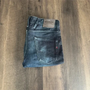 Replay Anbass jeans mörkblå, stl 30/34 - Snygga Replay Anbass jeans i mörkblå tvätt med diskreta slitningar och klassiska fem fickor. Jeansen har raka ben och röda detaljer vid fickan samt logga på bakfickan. Tillverkade i stretchig bomullsdenim för skön passform.