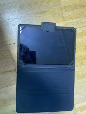 Android surfplatta med fodral - Snygg surfplatta med stor skärm, levereras med praktiskt fodral. Skärmen ser ut att vara i gott skick, inga synliga sprickor men några fingeravtryck. Perfekt för surf, film och appar. Modell och märke ej specificerat.